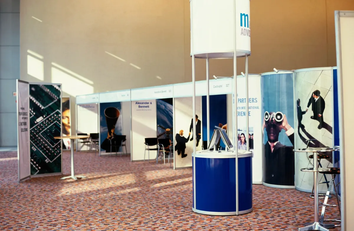 Indoor exhibition hall featuring modular booths, a central circular display stand, branded graphics and high tables under natural light